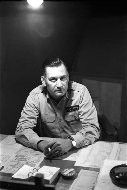 Military Man (Earl L. Denton name tag) sitting at desk, holding a cigarette.