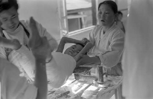 Man and woman putting child in body plaster.