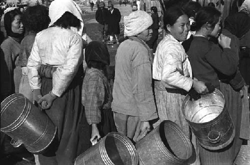 Women in line on street holding metal buckets