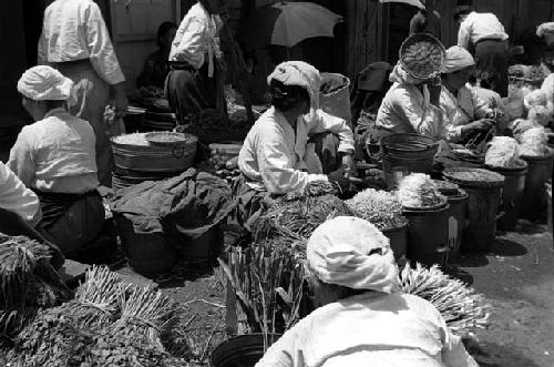 Women outdoors sitting with baskets of vegetables.