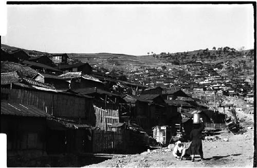 view of village with boy walking with pail on head in foreground