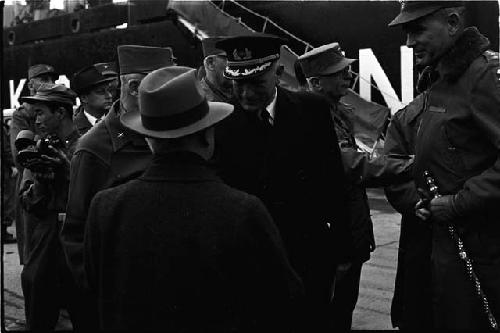 Man in hat facing men in officer uniforms on docks