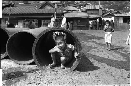 Small child squatting inside long hollow cylinder