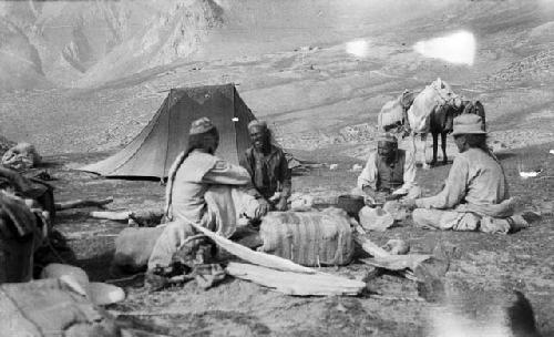 Four men sitting at campsite, supplies tent and loaded pack horses