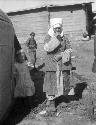 Older women with white headdresses, standing by a yurt with small girl