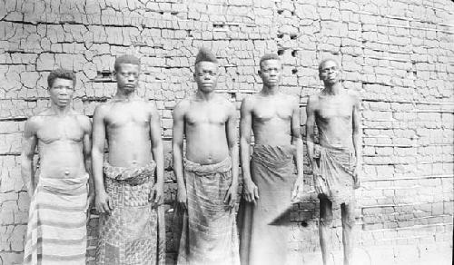 Front view of five men in front of brick building