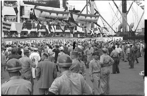 Large ship pulled up to dock and a crowd on the dock