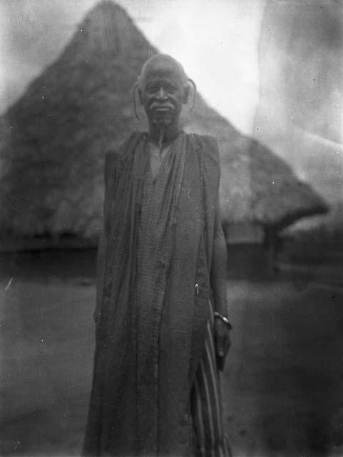 Elderly man, frontal view in front of hut