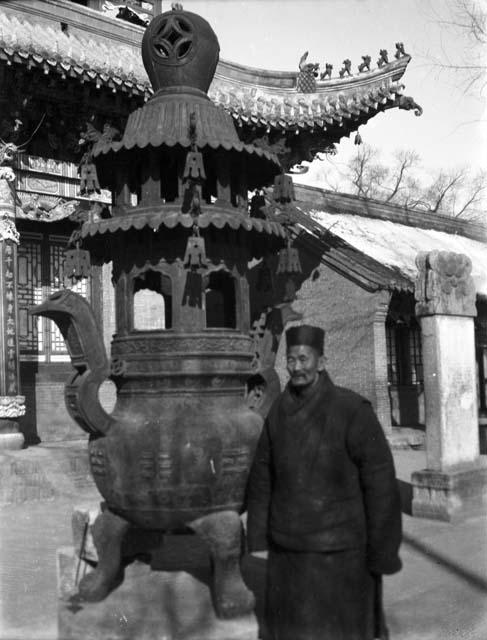 Portrait of a priest standing in front of a very large incense burner