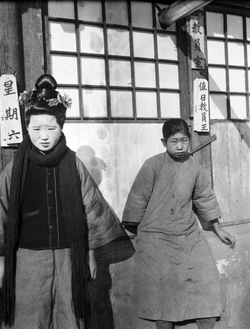 Marchu woman standing, boy sitting in front of school building with three signs