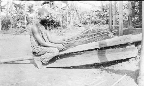 Man smoothing and shaping bark plates for hut