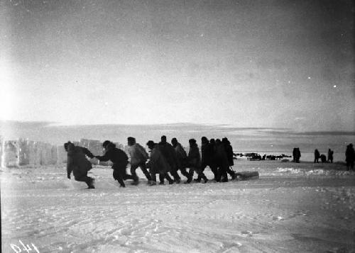 Dozen men dragging an ice block