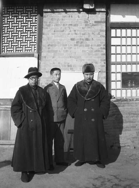 Portrait of three men stranding in front of a building, all in western dress