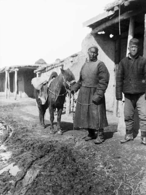 Older men standing next to pony in the street