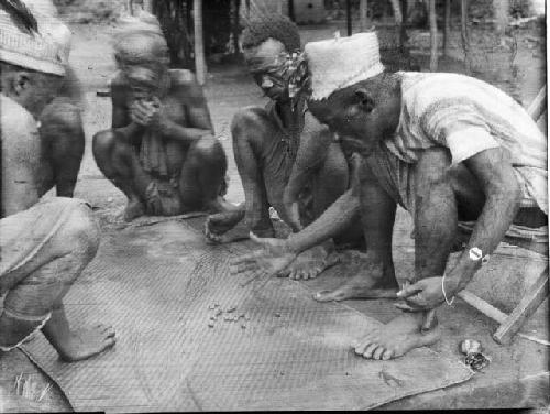 Men gambling around mat on ground