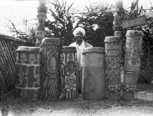 Man sitting behind a line of carved, decorated drums