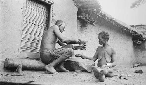 Man removing woman's bracelet with hammer and rock