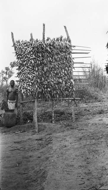 Man standing next to wooden rack for drying corn