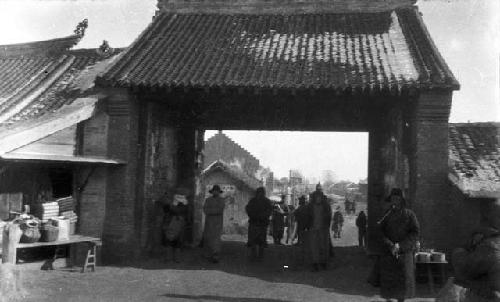 View of large open city gate with several people walking through