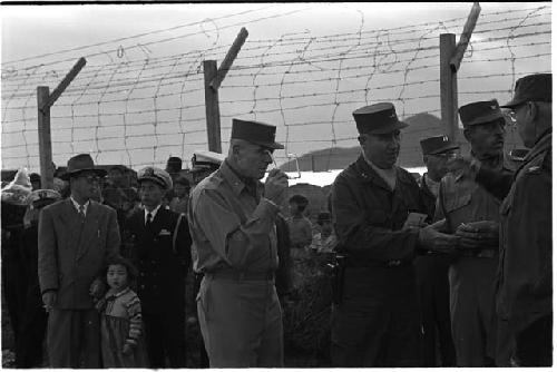 Military personnel standing next to a barbed wire fence