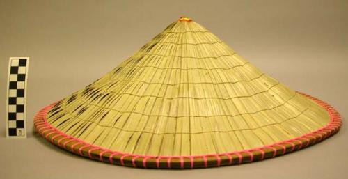 Woven hat, rim with pink plastic line, finial of thread and textile