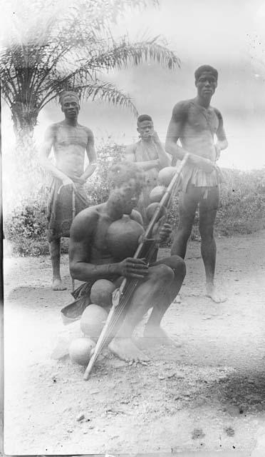 Man playing harp with other men standing behind him