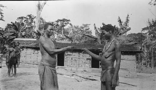 Man and woman greeting each other in front of hut