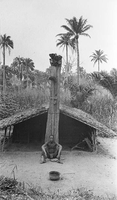 Man sitting in front of a Bafia hut
