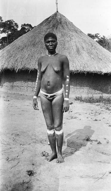 Women in mourning dress in front of hut, with painted arms and legs