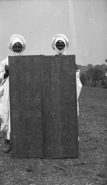 Two men holding carved wooden door panels