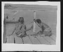 Two men seated on dock by water