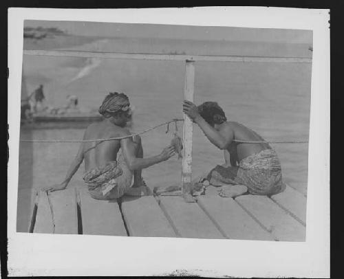 Two men seated on dock by water