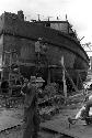 Men working on beams/structures in front of docked ship.