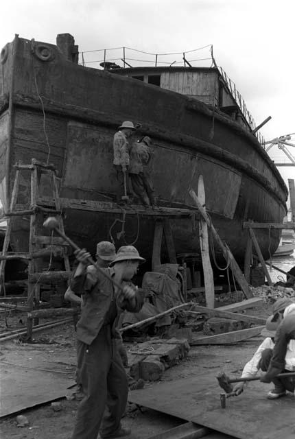 Men working on beams/structures in front of docked ship.