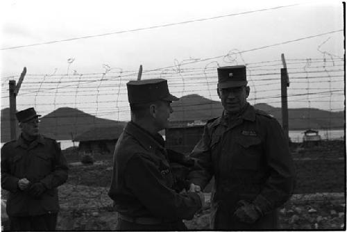 Military officers talking in front of a barbed wire fence