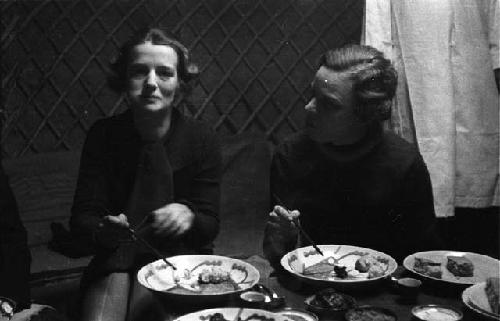 Eleanor Lattimore and woman sitting at table in yurt, eating