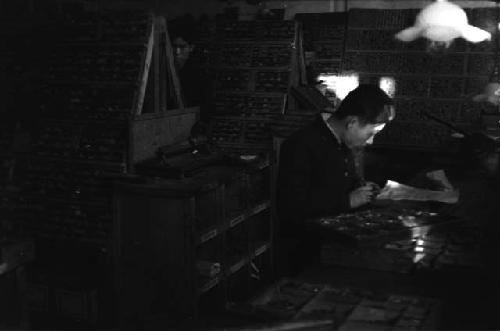 Chinese typesetter in newspaper office with racks of type