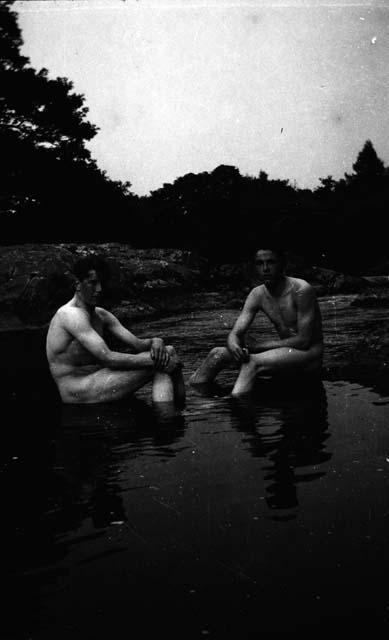 Two naked men sitting on rocks in water