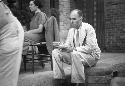 Man in suit and tie sitting, drinking out of teacups