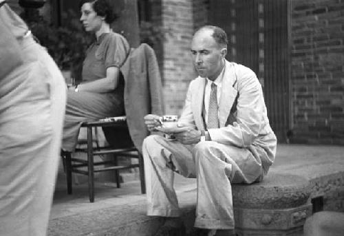 Man in suit and tie sitting, drinking out of teacups