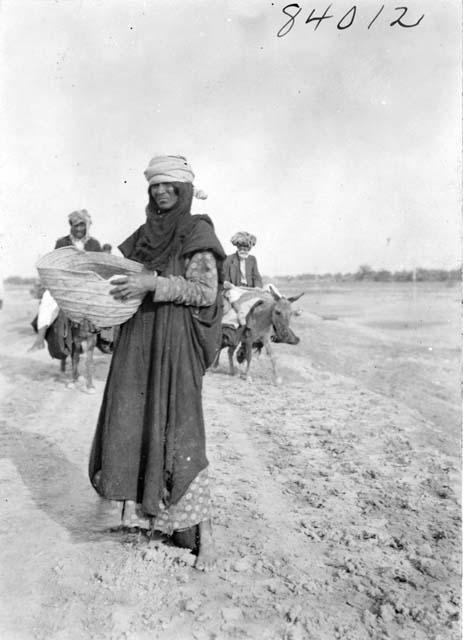 Portrait of woman with basket with men and donkeys in the background