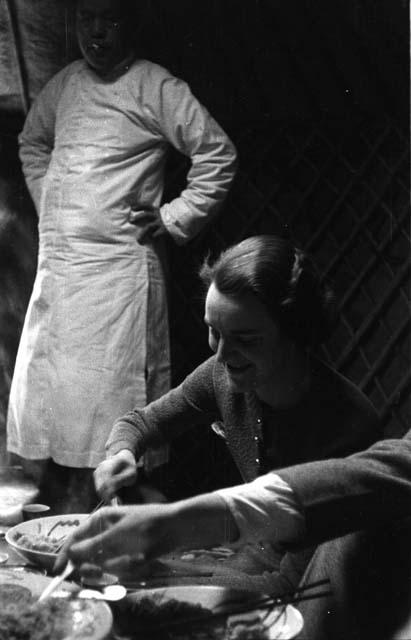 Woman seated at table eating, Moses standing behind