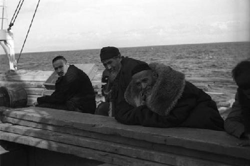 Three men, leaning onto wood boards on boat