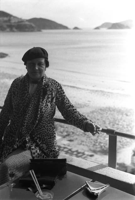 Western woman in leopard-skin coat wearing beret sitting on ledge by table