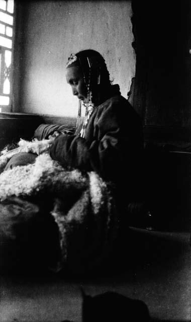 Woman with braids sitting next to window and sewing