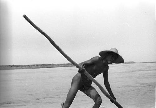 Naked man with a hat on holding a pole on the raft carring their car