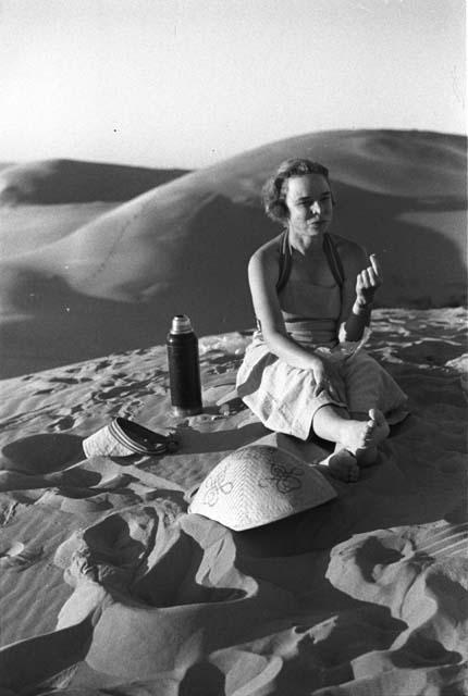 Eleanor Lattimore sitting in sand, eating and drinking