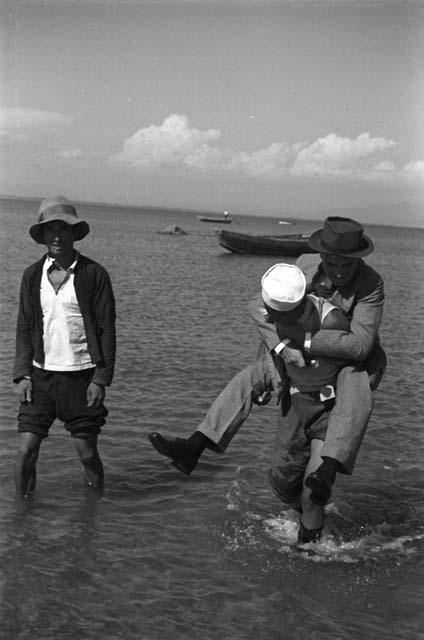 One man carrying another through shallow water