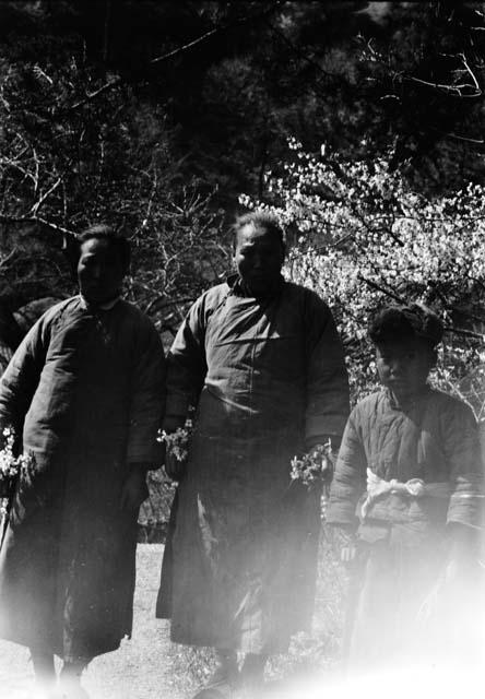 Two women holding flowers and a boy in a fur cap