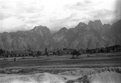 Landscape with trees, building on plateau and jagged mountains